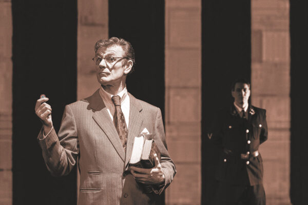 Ein Mann im Anzug mit alten Büchern in der Hand, im Hintergrund ein Mann in NS-Uniform. Foto: Bettina Frenzel